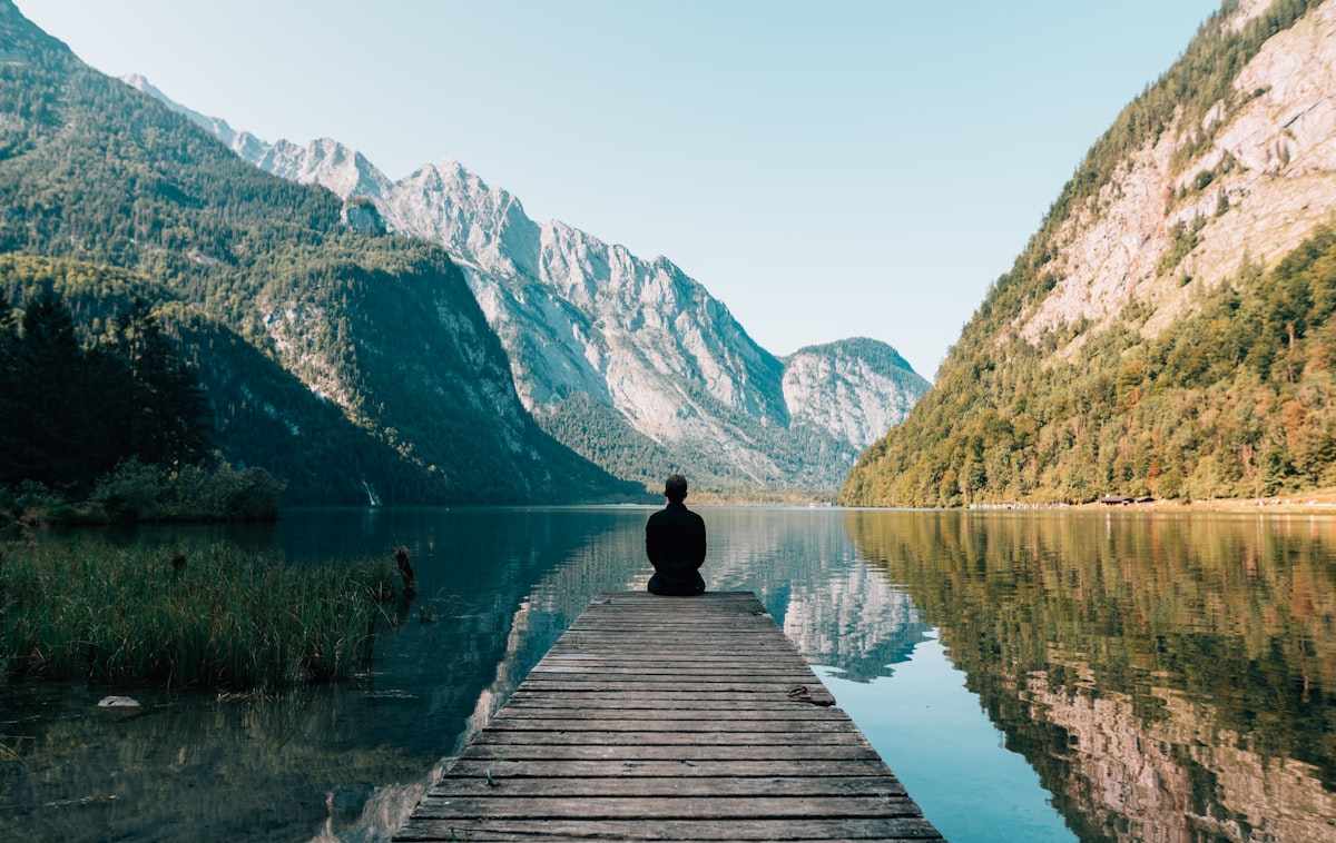 Mensch sitzt still auf einem Steg am Bergsee – Moment des Innehaltens und Tieferschauens